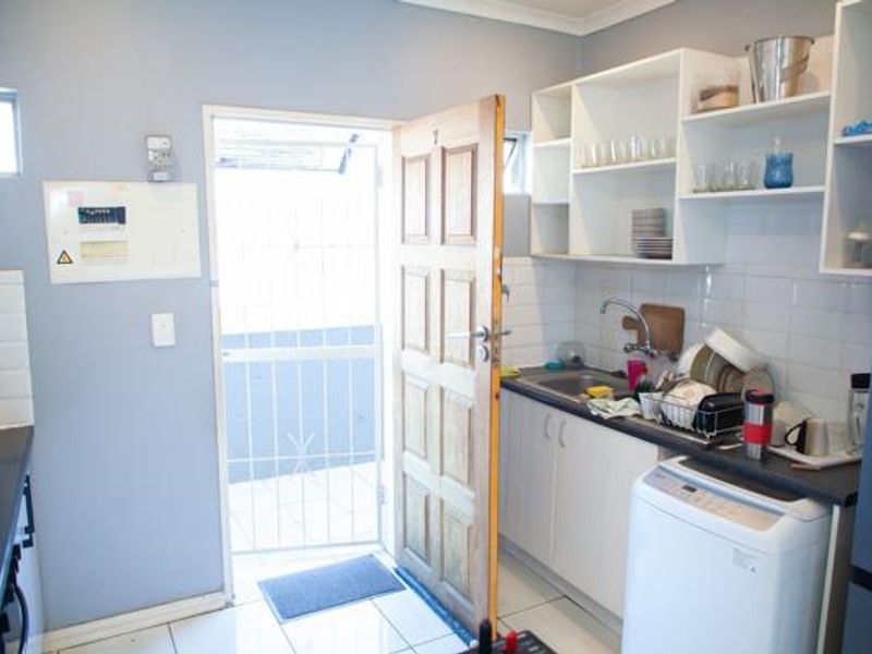 Functional scullery area featuring built-in cabinetry, stainless steel sink, tiled backsplash, and direct access to an exterior space via a security gate.