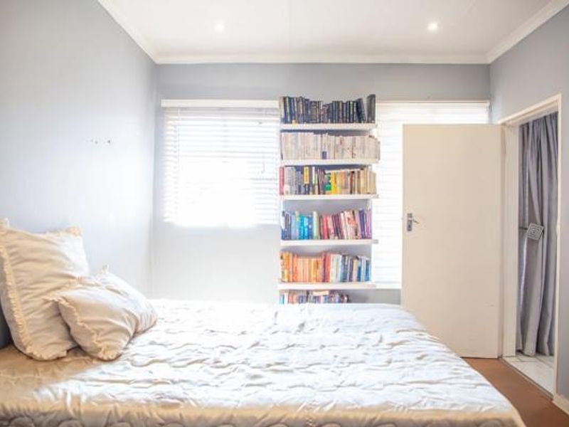 A bedroom featuring built-in shelving, venetian blinds, and recessed lighting, with neutral wall tones and a functional layout.