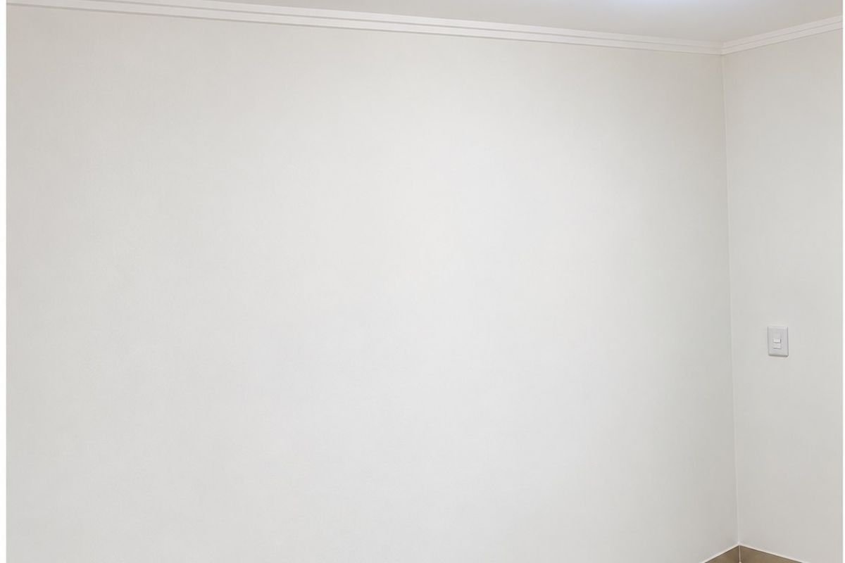 A clean, empty room featuring neutral tiled flooring, white walls with crown molding, and a modern flush-mount ceiling light.