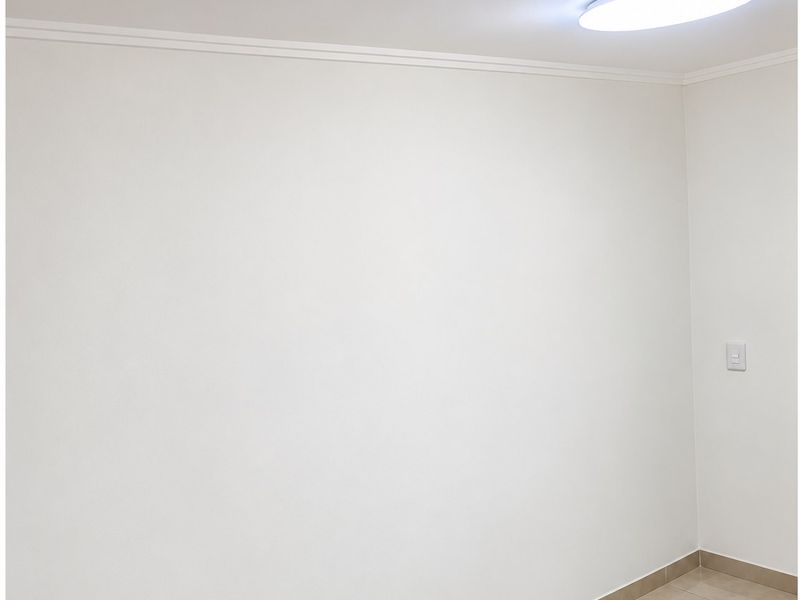 A clean, empty room featuring neutral tiled flooring, white walls with crown molding, and a modern flush-mount ceiling light.