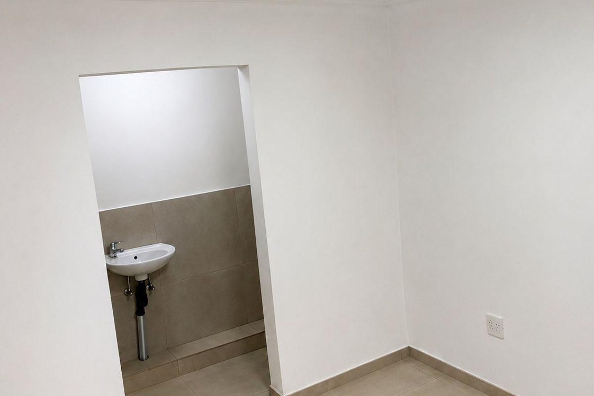 A clean, minimalist utility space featuring neutral ceramic floor tiles, a wall-mounted basin, and bright, modern lighting.