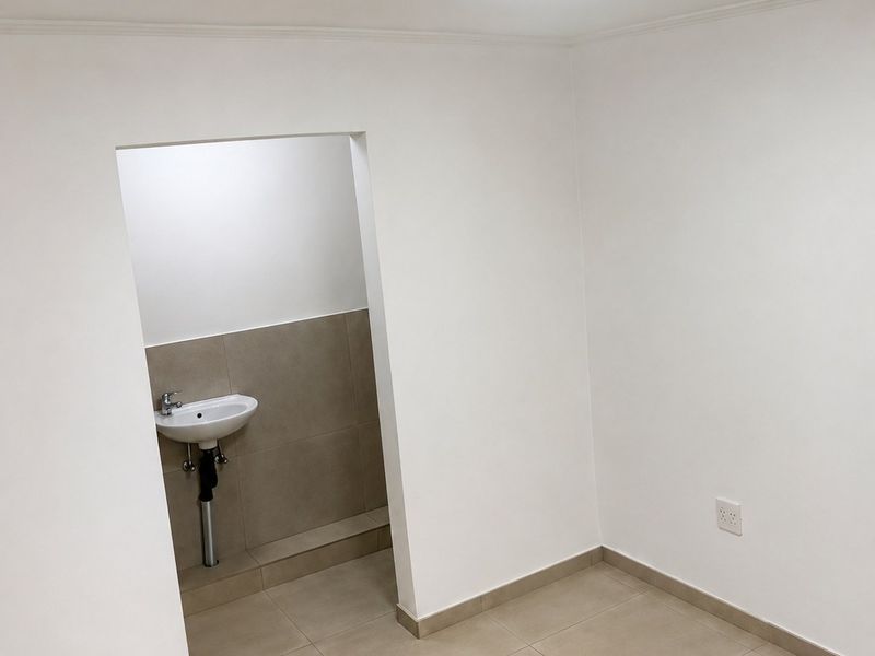 A clean, minimalist utility space featuring neutral ceramic floor tiles, a wall-mounted basin, and bright, modern lighting.