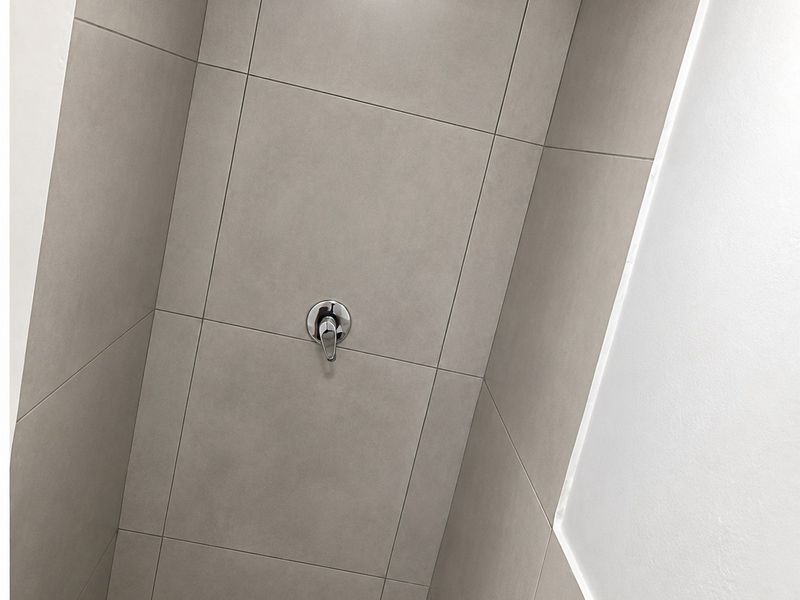 A modern shower enclosure featuring large format neutral wall tiles, a chrome shower mixer, and a fixed shower head.