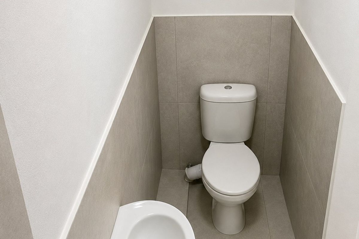 A clean, modern powder room featuring a white toilet and a wall-mounted basin with neutral ceramic tiling.