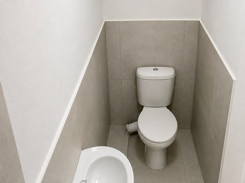 A clean, modern powder room featuring a white toilet and a wall-mounted basin with neutral ceramic tiling.