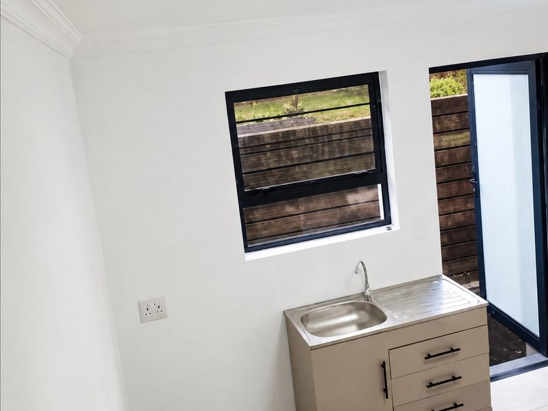 A clean, minimalist laundry area featuring a stainless steel sink, built-in cabinetry, tiled floors, and direct access to the exterior.