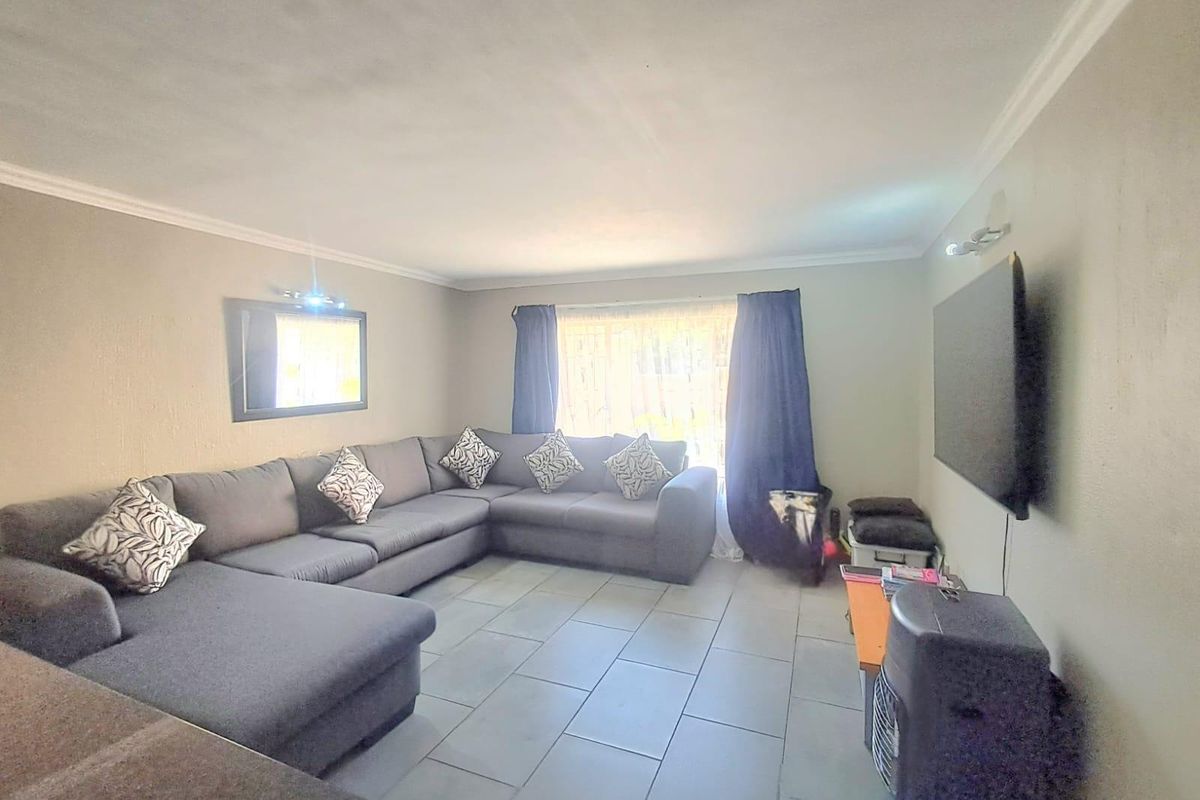 A spacious living room featuring neutral wall tones, tiled flooring, and decorative cove cornicing, providing a comfortable and functional area for relaxation.