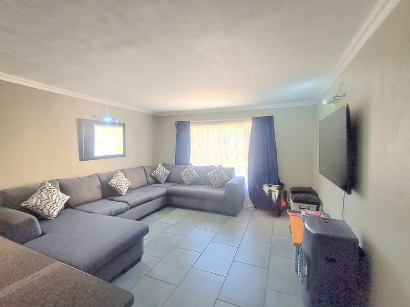 A spacious living room featuring neutral wall tones, tiled flooring, and decorative cove cornicing, providing a comfortable and functional area for relaxation.