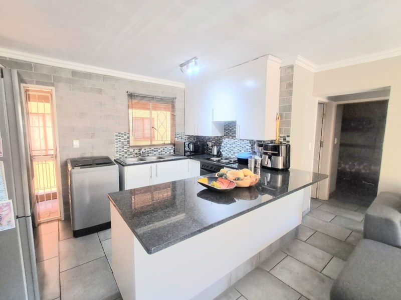 Modern kitchen featuring granite countertops, white cabinetry, tiled backsplash, and a functional layout with an integrated breakfast bar.