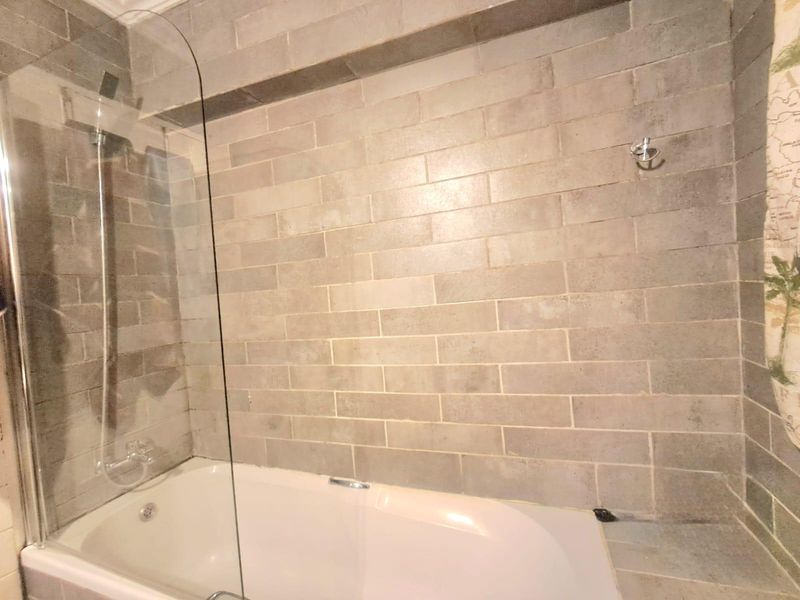 A modern bathroom featuring a bathtub with a glass shower screen and neutral-toned brick-style wall tiling.
