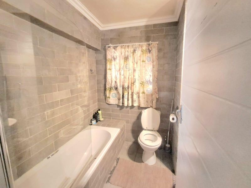 A functional bathroom featuring grey subway-style wall tiles, a built-in bathtub with a glass screen, and a standard toilet.