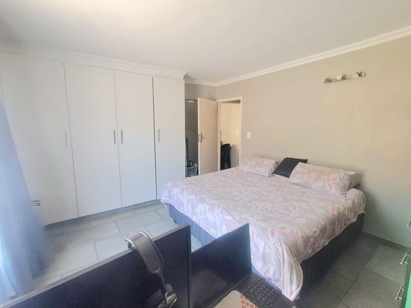 A bedroom featuring built-in cupboards, tiled flooring, and neutral wall finishes, providing a functional and well-lit sleeping space.