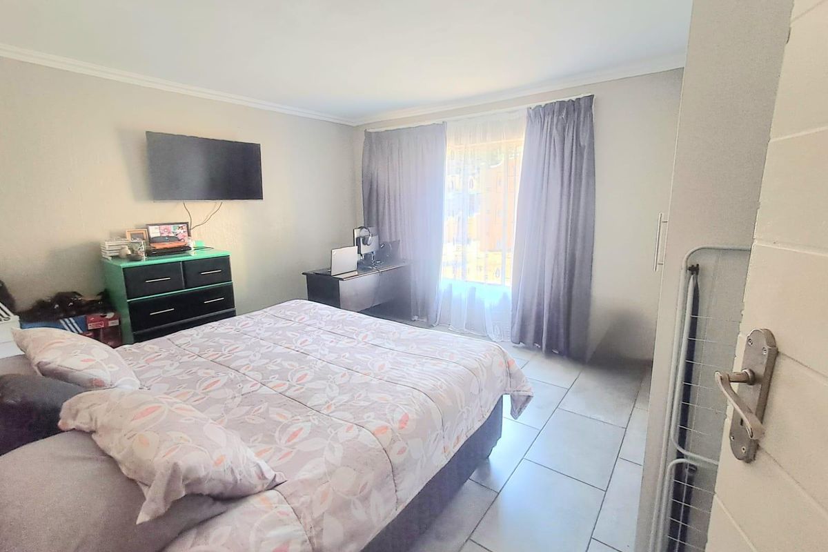 A functional bedroom featuring tiled flooring, built-in storage, and natural light through a window with curtains.