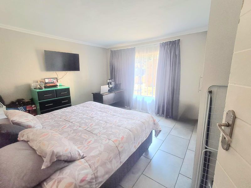 A functional bedroom featuring tiled flooring, built-in storage, and natural light through a window with curtains.