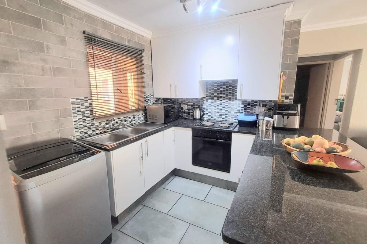 A functional kitchen featuring white cabinetry, dark granite countertops, a mosaic tile backsplash, and built-in oven and hob.