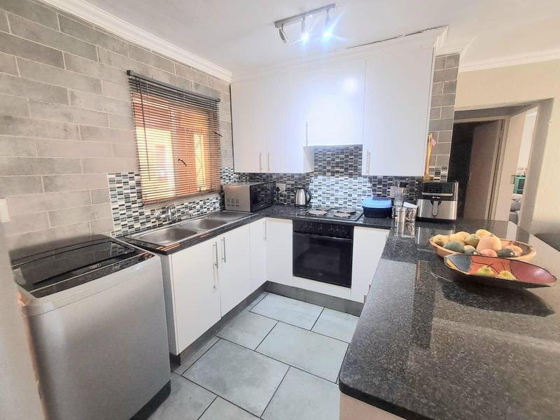 A functional kitchen featuring white cabinetry, dark granite countertops, a mosaic tile backsplash, and built-in oven and hob.