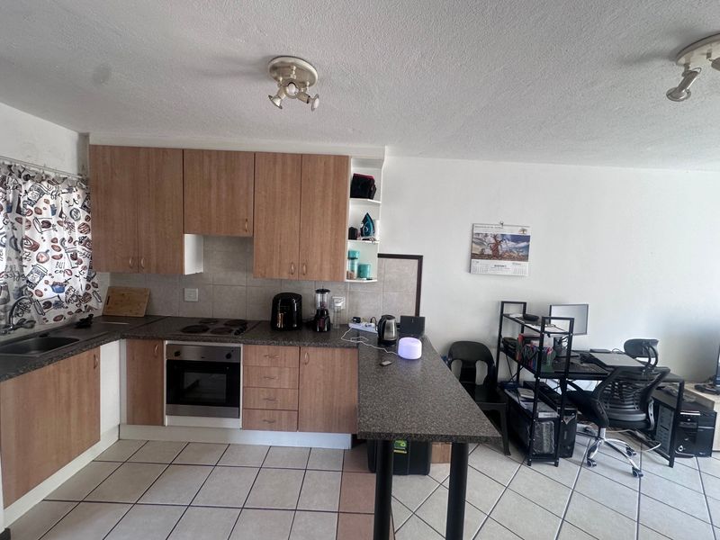 Open plan kitchen featuring laminate cabinetry, built-in oven, electric hob, and a breakfast bar, seamlessly flowing into a multi-purpose living and workspace area.