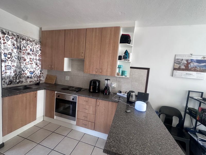 Functional kitchen featuring wood-look cabinetry, granite-style countertops, built-in oven, electric hob, and a convenient breakfast bar with tiled flooring.