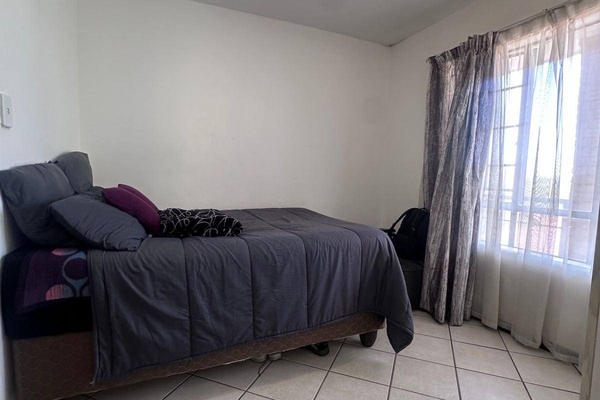 A functional bedroom featuring tiled flooring, a central ceiling light fixture, and large windows with curtain tracks for natural light.