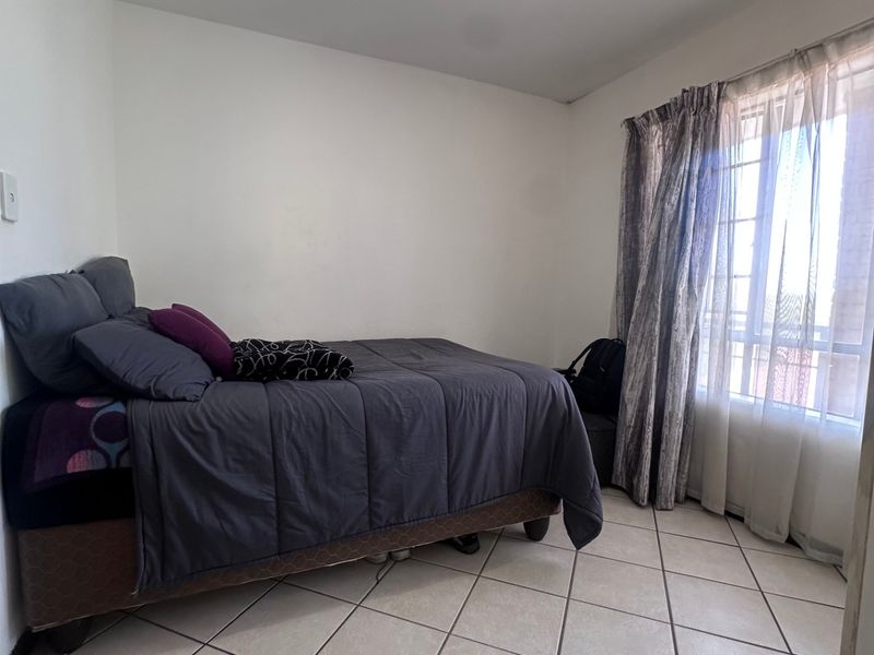 A functional bedroom featuring tiled flooring, a central ceiling light fixture, and large windows with curtain tracks for natural light.