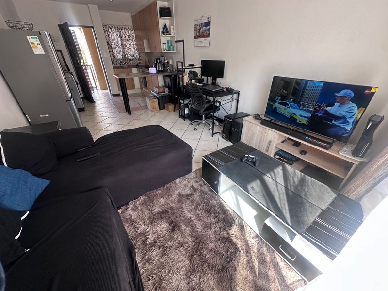 Open-plan living area featuring tiled flooring and a compact kitchen with built-in cabinetry and a breakfast counter.