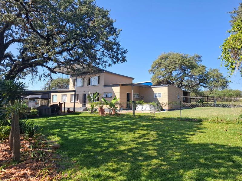 Rear view of a farm property featuring a brick dwelling with a metal roof, covered patio area, and expansive green garden.