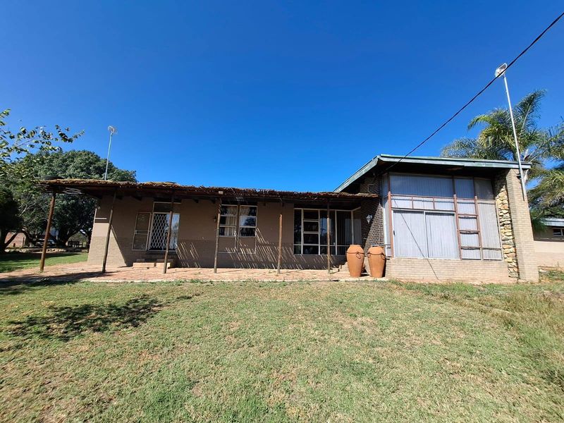 Rear view of the farmhouse featuring a large paved patio area with a thatched roof covering and expansive windows overlooking the garden.
