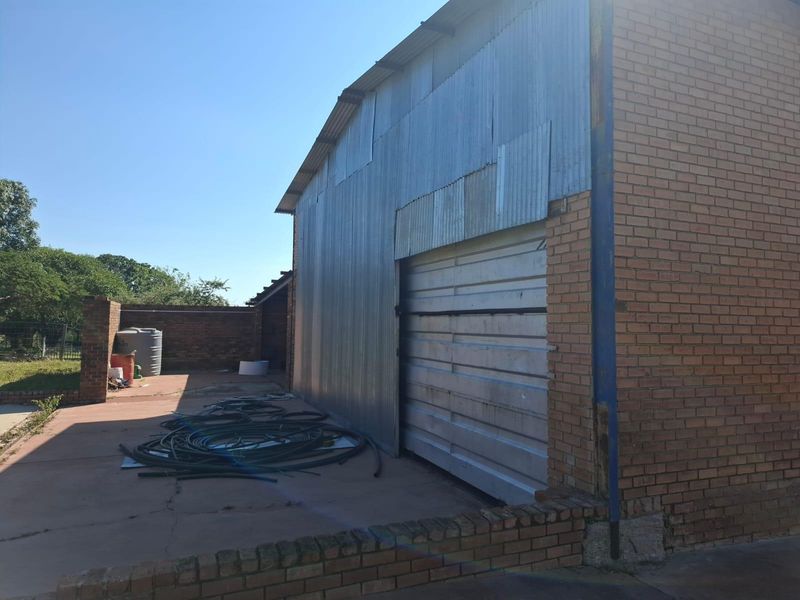 Rear view of a farm outbuilding featuring corrugated metal cladding, a large roller shutter door, and an adjacent concrete yard area.