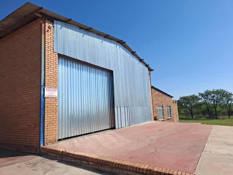Large industrial-style farm garage featuring a high corrugated metal roller door, face brick construction, and a concrete apron.