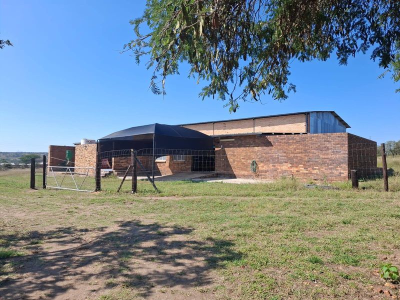 Rear view of a face brick farm building featuring a corrugated metal roof, fenced perimeter, and surrounding open land.