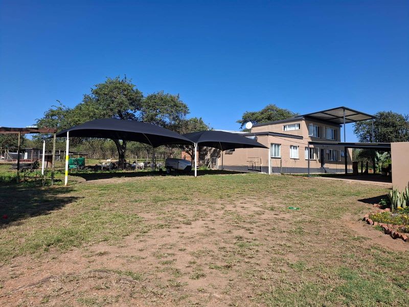 Rear view of a farm property featuring a multi-level structure with a metal roof, shade sail structures, and surrounding garden area.