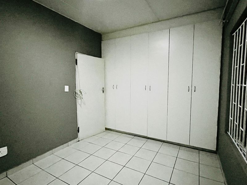 A simple bedroom featuring white built-in cupboards, tiled flooring, and security bars on the window.