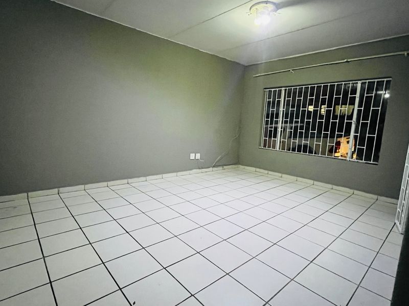 An empty living room featuring tiled flooring and a window fitted with security bars.