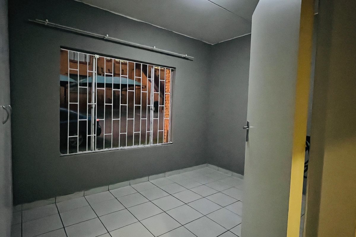 An empty bedroom featuring tiled flooring, built-in cupboards, and security bars on the window.