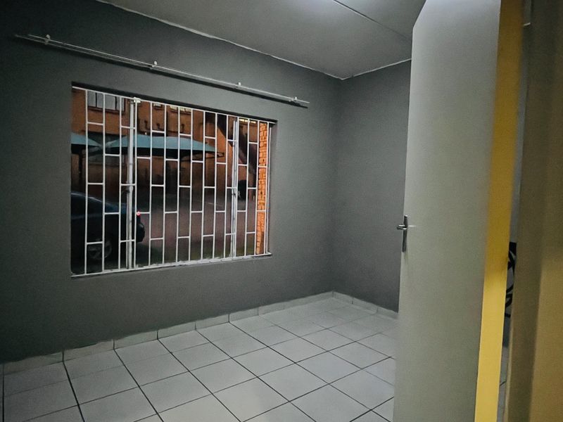 An empty bedroom featuring tiled flooring, built-in cupboards, and security bars on the window.