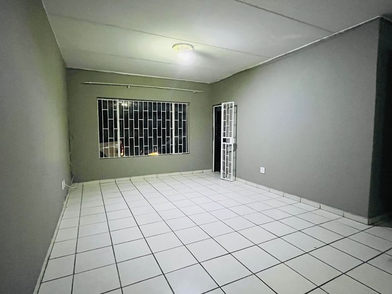 An empty, neutrally painted living area featuring tiled flooring, security gate, and burglar bars on the window.
