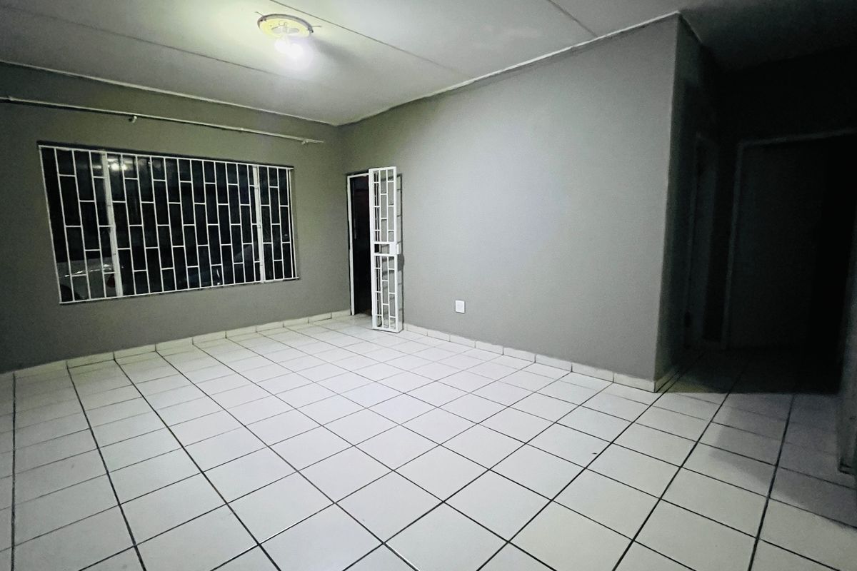 An empty living room featuring tiled flooring, security bars on the window, and a security gate, providing a blank canvas for interior design.