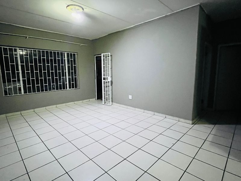 An empty living room featuring tiled flooring, security bars on the window, and a security gate, providing a blank canvas for interior design.