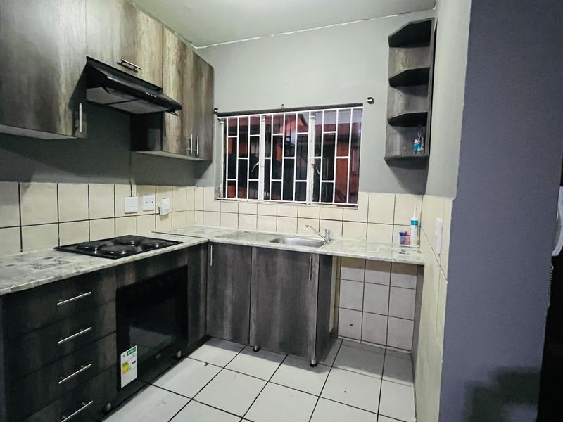 A functional kitchen featuring dark wood-look cabinetry, built-in oven and hob, tiled backsplash, and tiled flooring with security bars on the window.