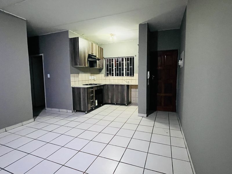 Open plan living area featuring a compact kitchen with built-in cabinetry, tiled flooring, and security bars on the window.