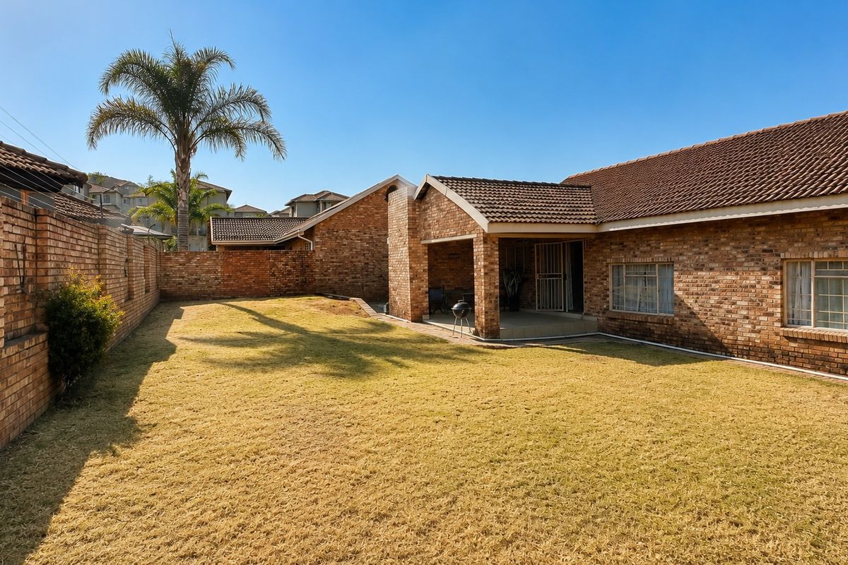 Spacious rear garden featuring a face brick townhouse exterior, a covered patio area, and secure window treatments.