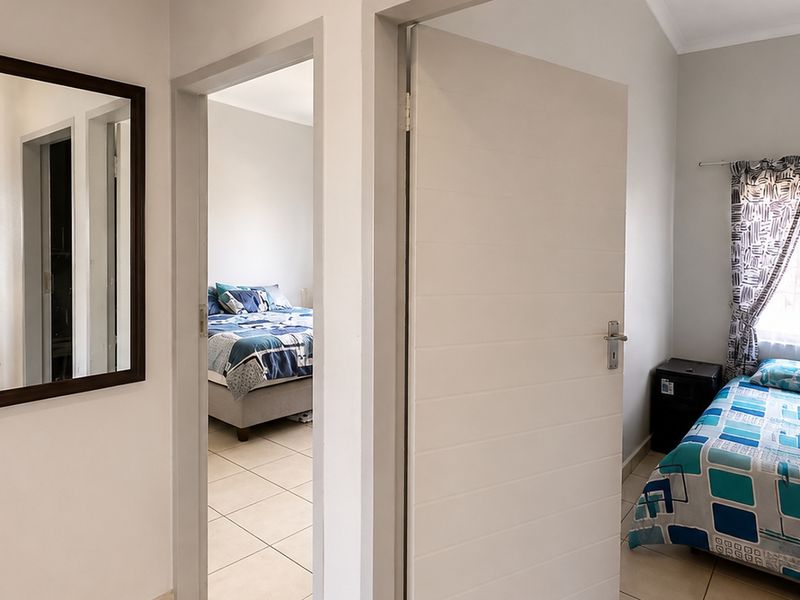 A bright hallway connecting multiple rooms, featuring neutral tiled flooring and clean white interior doors.