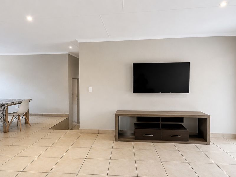 Spacious open-plan living and dining area featuring neutral wall tones, ceramic floor tiles, and direct access to the outdoor space through a sliding glass door.