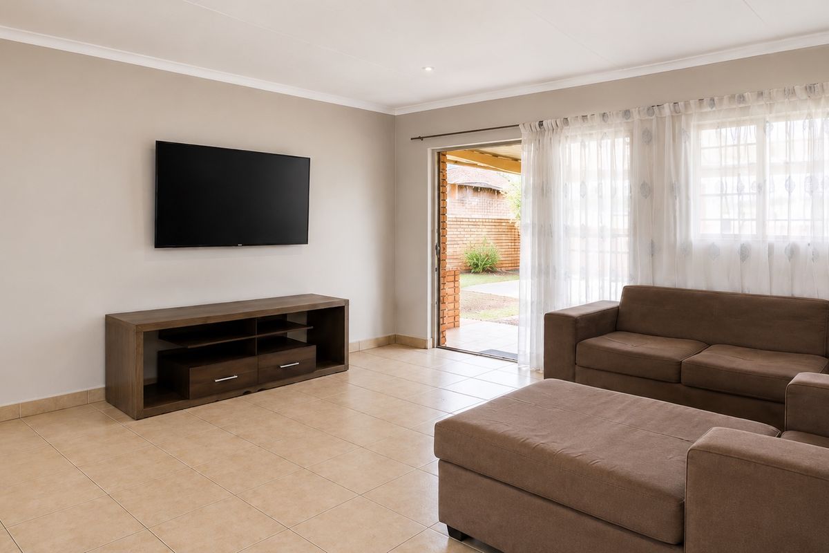 A bright and spacious living room featuring neutral tiled flooring, cove cornicing, and a sliding glass door providing direct access to the outdoor patio area.