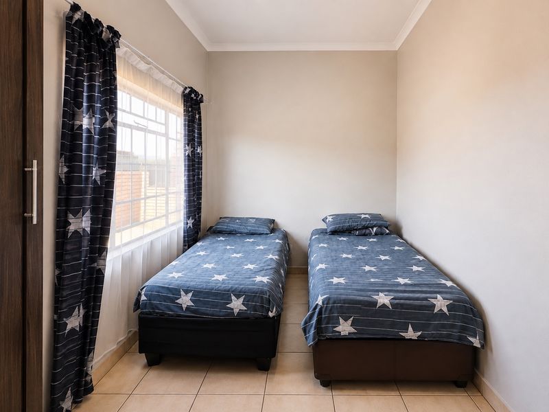 A neat bedroom featuring tiled flooring, a built-in cupboard, and a window fitted with security burglar bars.