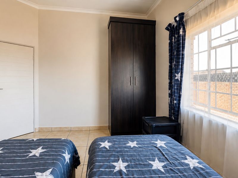 A functional bedroom featuring tiled flooring, a built-in cupboard, and a window with security bars, offering a clean and practical living space.