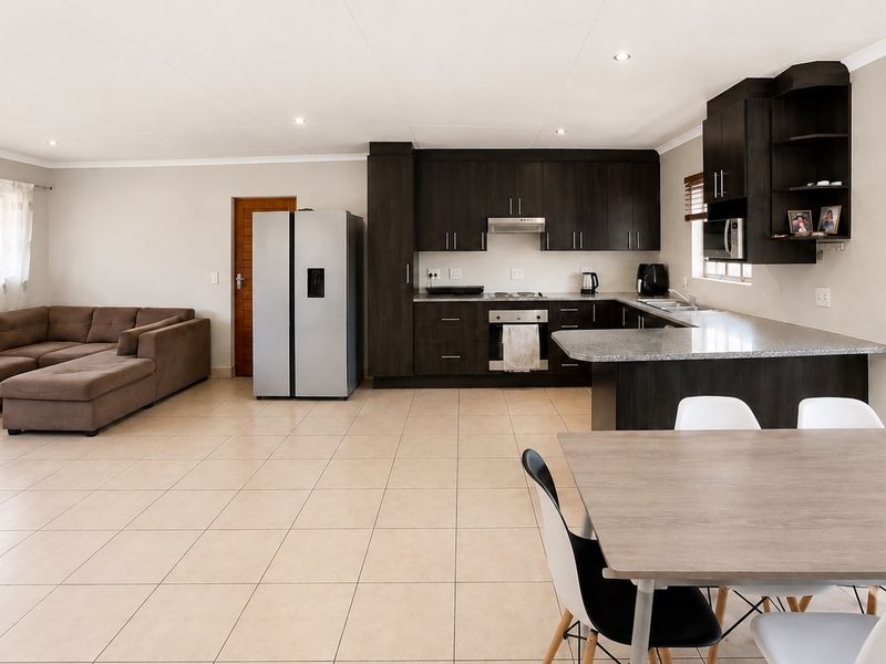 Spacious open-plan living area featuring a modern kitchen with dark cabinetry, granite countertops, and integrated appliances, flowing seamlessly into the dining and lounge space.