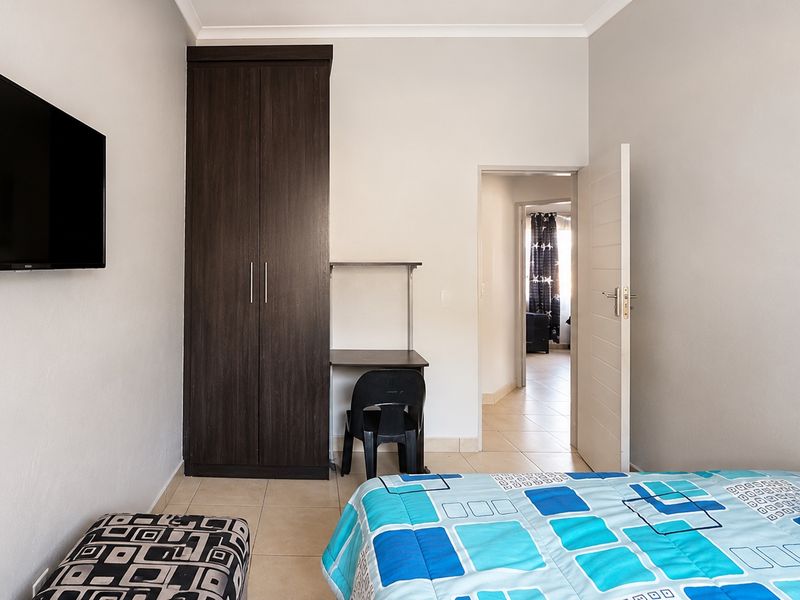 A functional bedroom featuring tiled flooring, a built-in wardrobe, and neutral wall finishes, providing a clean and practical living space.