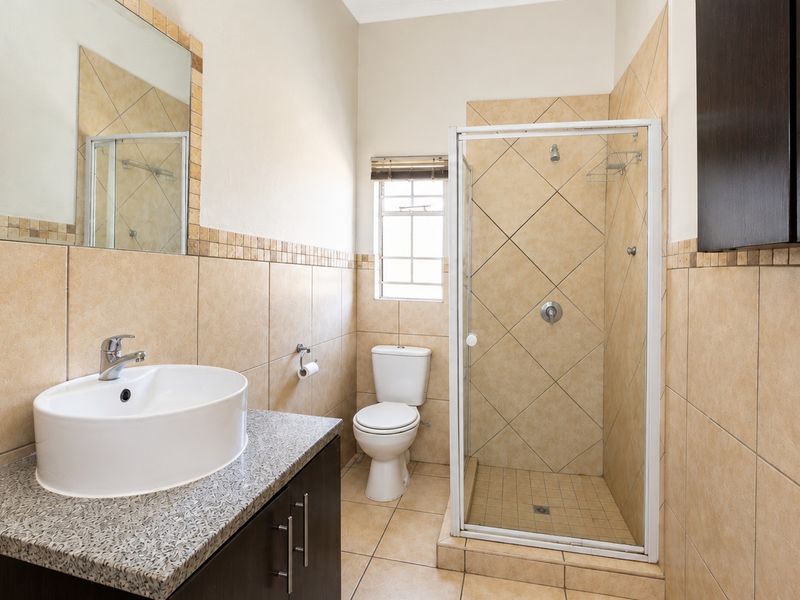 A clean, functional bathroom featuring a vessel sink on a granite vanity, a glass-enclosed shower, and neutral wall and floor tiling.