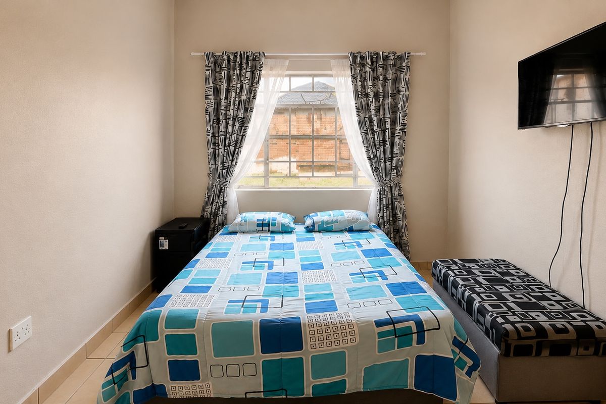 A functional bedroom featuring tiled flooring, a central window, and wall-mounted television space.